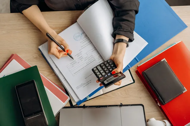 Contador analisando documentos financeiros com uma calculadora sobre a mesa de trabalho.