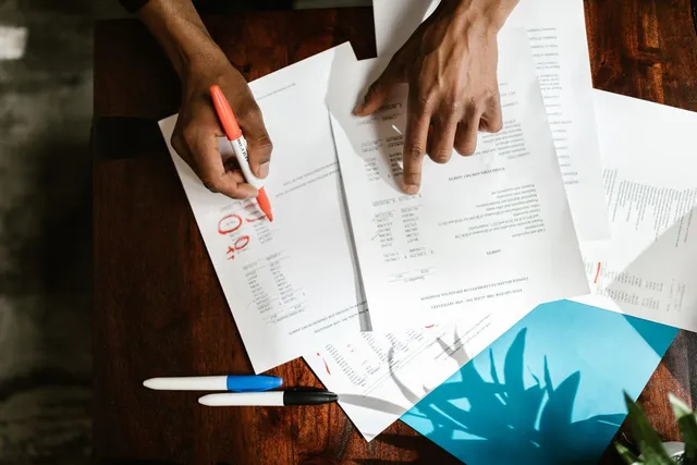 Mãos revisando e marcando documentos impressos sobre uma mesa de madeira
