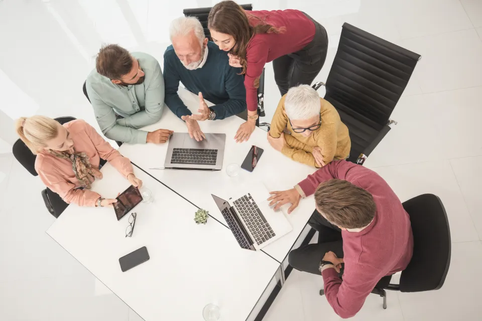 Vista de cima de uma equipe reunida ao redor de uma mesa de escritório com dois notebooks e documentos